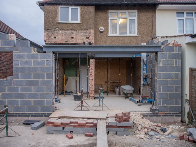 The back of a house is under construction, with partially built cinderblock walls and sundry construction materials scattered around.